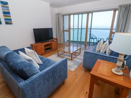 A living room with blue sofas a wooden coffee table a flat screen tv on a stand and a balcony overlooking the sea at Kittiwake in Carbis Bay