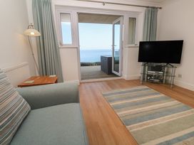 A living room with a TV and door leading to a view at Sapphire in Carbis Bay