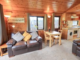 A living room with a sofa, dining table, and kitchen unit at Squirrels Leap, Number 29, Burnside Park near Keswick