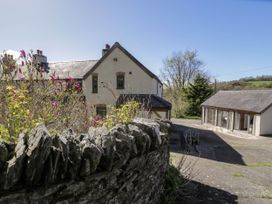 A rural property with a stone wall a main house and an outbuilding surrounded by trees and hills at Fron Goch Farm in Llanfair Talhaiarn