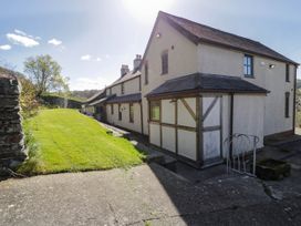 A side view of a two-story house with a sloped roof and lawn next to a stone wall at Fron Goch Farm in Llanfair Talhaiarn