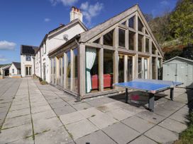 A large house with a glass conservatory red sofas inside a blue ping pong table outside and a small shed at Fron Goch Farm in Llanfair Talhaiarn