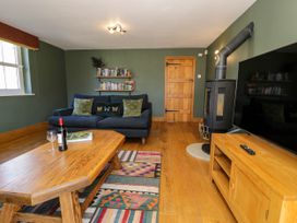 A living room with a wooden door a black stove a blue sofa with pillows a wooden coffee table with a wine bottle and glass a colorful rug and a wooden TV stand with a remote at Fron Goch Farm Llanfair Talhaiarn