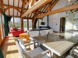 A room with wooden beams and wicker dining table with chairs and sofas near large windows at Fron Goch Farm Llanfair Talhaiarn