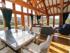 A dining area with a glass table and wicker chairs next to a living room with sofas and large windows at Fron Goch Farm in Llanfair Talhaiarn
