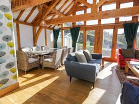 A living room with wooden beams wicker dining chairs sofas and large windows with green curtains at Fron Goch Farm in Llanfair Talhaiarn