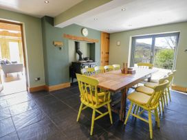 A dining room with a wooden table and yellow chairs near a wood stove and large glass doors at Fron Goch Farm in Llanfair Talhaiarn
