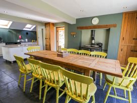 A dining area with a wooden table surrounded by yellow chairs and a kitchen in the background at Fron Goch Farm Llanfair Talhaiarn