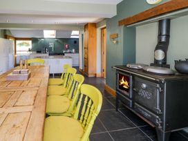 A kitchen with a wooden dining table and yellow chairs next to a black wood stove at Fron Goch Farm in Llanfair Talhaiarn