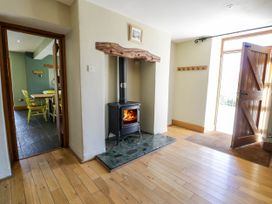 A hallway with a wood burning stove and wooden floor next to an open wooden door and an adjacent dining area with yellow chairs at Fron Goch Farm in Llanfair Talhaiarn