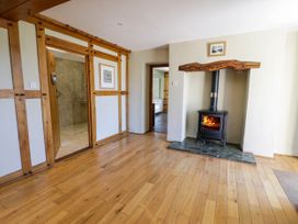 A room with wooden floors a wood burning stove in a fireplace and an open doorway showing a tiled bathroom at Fron Goch Farm in Llanfair Talhaiarn