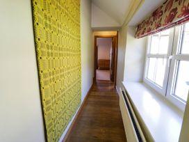 A hallway with wooden flooring a yellow patterned wall hanging a window with red patterned blind and a radiator at Fron Goch Farm Llanfair Talhaiarn