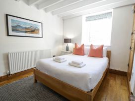A bedroom with a wooden bed and white bedding topped with two coral pillows two folded towels on the bed a window with a floral blind a bedside table with a lamp a framed landscape picture on the wall and a patterned rug on a wooden floor at Fron Goch Farm in Llanfair Talhaiarn