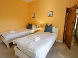 A bedroom with two single beds with white bedding and dark pillows a bedside table with a lamp and two framed pictures on the wall at Fron Goch Farm Llanfair Talhaiarn