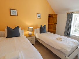 A bedroom with two single beds a nightstand with a lamp wooden door and a window with curtains at Fron Goch Farm Llanfair Talhaiarn