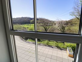 A view of a tiled patio with a metal fence and a planter outside a window overlooking trees and hills at Fron Goch Farm in Llanfair Talhaiarn