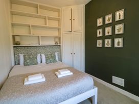 A bedroom with a bed with green pillows and a patterned headboard beside white shelves and a green wall with framed plant pictures at Fron Goch Farm in Llanfair Talhaiarn