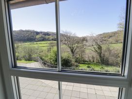 A view of a tiled patio and green fields with trees and hills through a window at Fron Goch Farm in Llanfair Talhaiarn