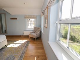 A room with a beige armchair a rug wooden floor and two windows at Fron Goch Farm in Llanfair Talhaiarn