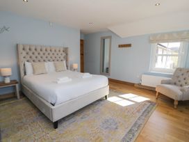 A bedroom with a large bed, two bedside tables with lamps, a wall mirror, an armchair, and a window at Fron Goch Farm in Llanfair Talhaiarn