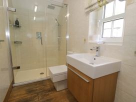 A bathroom with a glass shower enclosure a toilet and a sink with a wooden cabinet and a window with striped blinds at Fron Goch Farm in Llanfair Talhaiarn