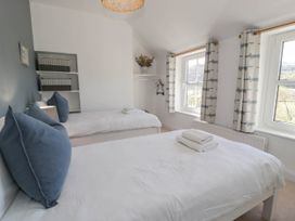 A bedroom with two single beds side by side under two windows with patterned curtains and a shelf with storage boxes at Fron Goch Farm Llanfair Talhaiarn