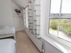A bedroom with two single beds a window with patterned curtains and a vase with dried flowers on a shelf at Fron Goch Farm in Llanfair Talhaiarn
