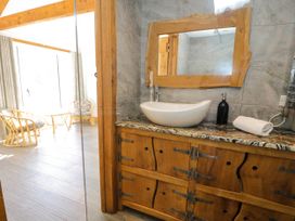 A bathroom sink with a wooden framed mirror and wooden cabinet next to a sunlit room with wicker chairs at Fron Goch Farm in Llanfair Talhaiarn