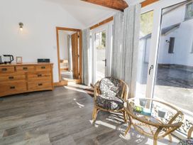 A room with a wooden dresser a floral cushioned chair a glass top table and large windows at Fron Goch Farm in Llanfair Talhaiarn