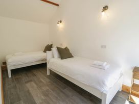 A bedroom with two single beds with white linens and green pillows a small wooden nightstand and wall lights at Fron Goch Farm in Llanfair Talhaiarn