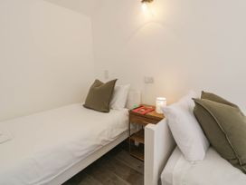 A bedroom with two single beds a wooden nightstand a small lamp and books at Fron Goch Farm in Llanfair Talhaiarn