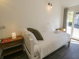 A bedroom with single bed white linens wooden bedside tables lamp and glass door at Fron Goch Farm in Llanfair Talhaiarn
