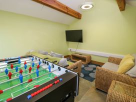 A game room with a foosball table sofas a wall-mounted television and a wicker table at Fron Goch Farm in Llanfair Talhaiarn