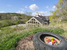 A large farmhouse with chimneys and a glass extension surrounded by countryside and a tire sandbox with children's toys in the foreground at Fron Goch Farm in Llanfair Talhaiarn