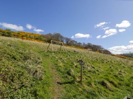 A grassy hillside with a wooden swing set picnic table and a wooden signpost at Fron Goch Farm in Llanfair Talhaiarn