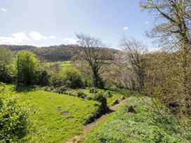 A grassy garden with a dirt path and trees overlooking hills at Fron Goch Farm in Llanfair Talhaiarn