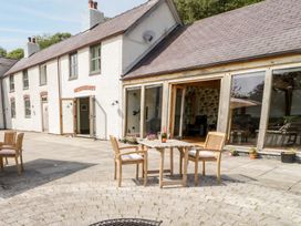 An outdoor patio area with wooden chairs and table outside a white building with large glass doors at Fron Goch Farm in Llanfair Talhaiarn