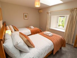 A bedroom with two beds, window, and bedside lamp at Swallow's Nest Thornthwaite near Braithwaite