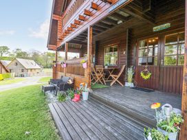 A wooden porch with chairs tables flower pots and a wreath on the door at Sun View Lodge in Llanbedr