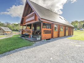 A wooden lodge with a covered porch and outdoor seating on a gravel and grass area at Sun View Lodge in Llanbedr