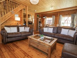 A living room with two brown leather sofas a wooden coffee table and dining area in a wooden cabin at Sun View Lodge in Llanbedr