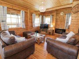 A living room with brown sofas, a glass coffee table, a television, and windows with curtains at Sun View Lodge in Llanbedr