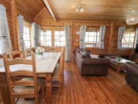 A wooden dining table with chairs and a small flower arrangement next to a seating area with brown leather sofas in a wooden cabin at Sun View Lodge in Llanbedr