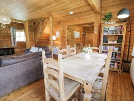 A wooden dining table with six chairs and a flower vase in a wooden walled living room with sofas and a bookshelf at Sun View Lodge in Llanbedr