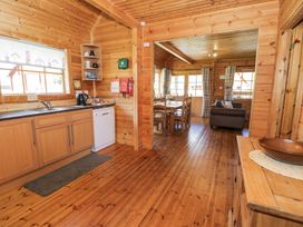 A wooden kitchen with cabinets a sink dishwasher and kettle next to a dining area with a table chairs and a sofa at Sun View Lodge Llanbedr