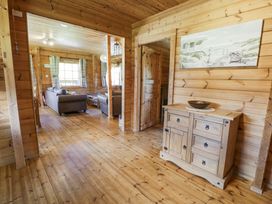 A wooden hallway with a wooden cabinet and a painting on the wall leading to a living room with sofas and a window at Sun View Lodge in Llanbedr
