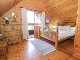 A wooden bedroom with a bed pillows a dresser a mirror and a door leading to a balcony at Sun View Lodge Llanbedr