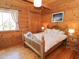 A bedroom with a wooden bed and white bedding two bedside tables with lamps and a window with curtains at Sun View Lodge in Llanbedr