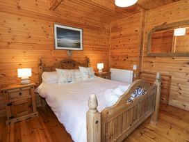 A wooden bedroom with a double bed two bedside tables with lamps a large mirror on the wall and a framed picture at Sun View Lodge in Llanbedr