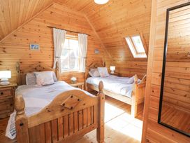 A wooden bedroom with two single beds bedside tables a window with curtains and a skylight at Sun View Lodge in Llanbedr